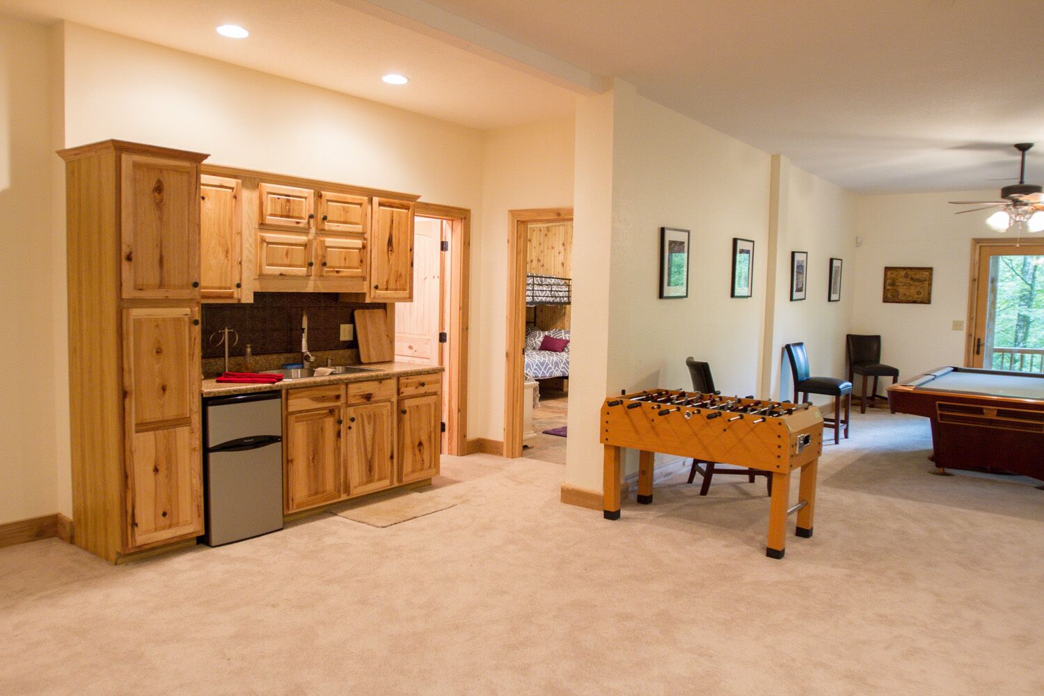 A spacious kitchen with wooden cabinets, a built-in refrigerator, and a foosball table in a living area with a pool table and comfortable seating.