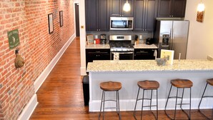 A modern kitchen with dark cabinets, a stainless steel refrigerator, a microwave, and a granite countertop. There are four bar stools at the island.