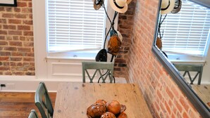 A wooden dining table with chairs, a bowl of bread, and a brick wall.