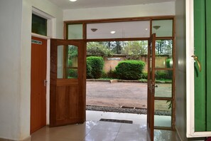 A hotel entrance with a wooden door and glass panels, leading to a courtyard with a paved area and greenery. - Westwood Hotel Nyeri (Nyeri)