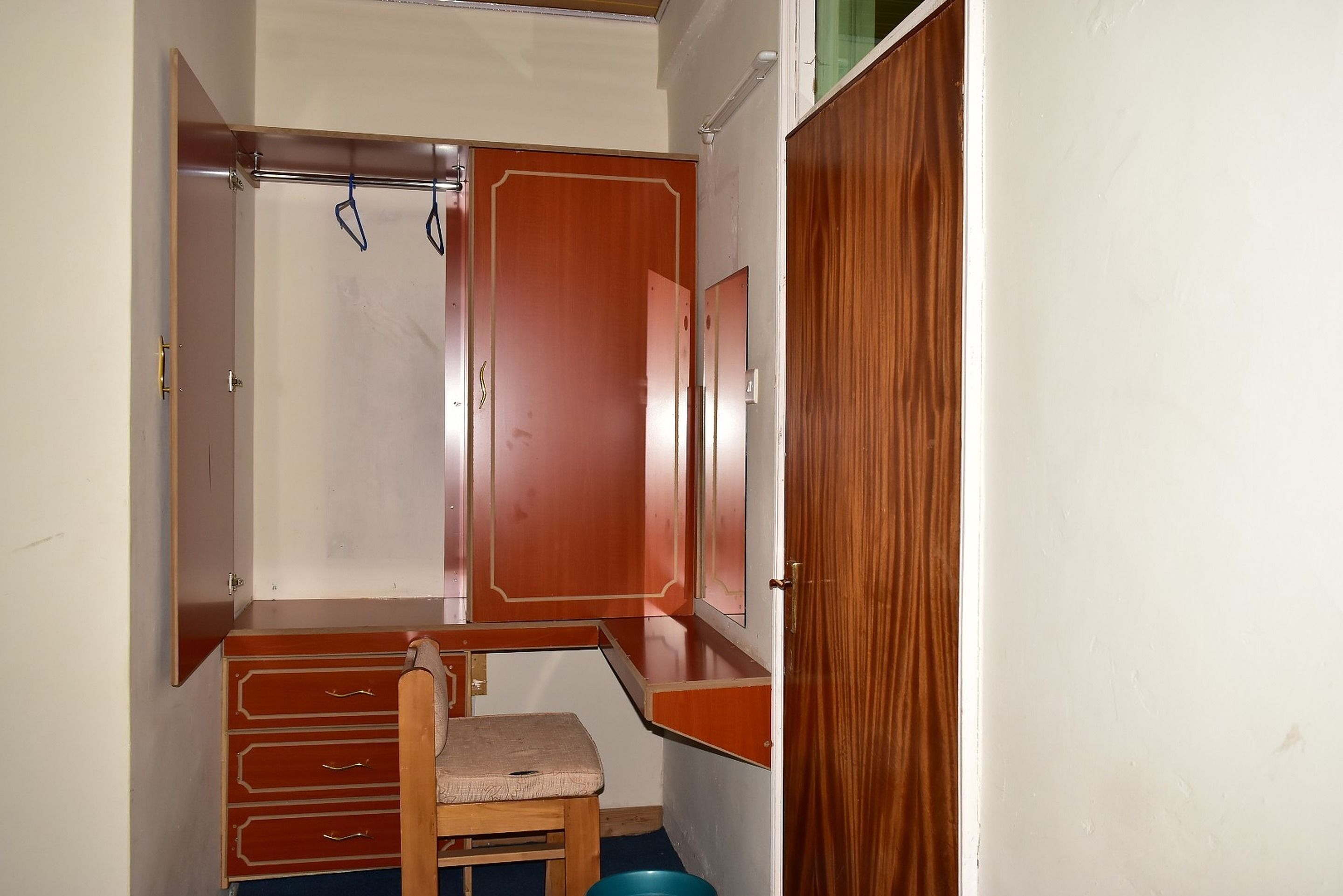 Una habitación compacta con un armario de madera, un pequeño banco y un tazón azul en el suelo.