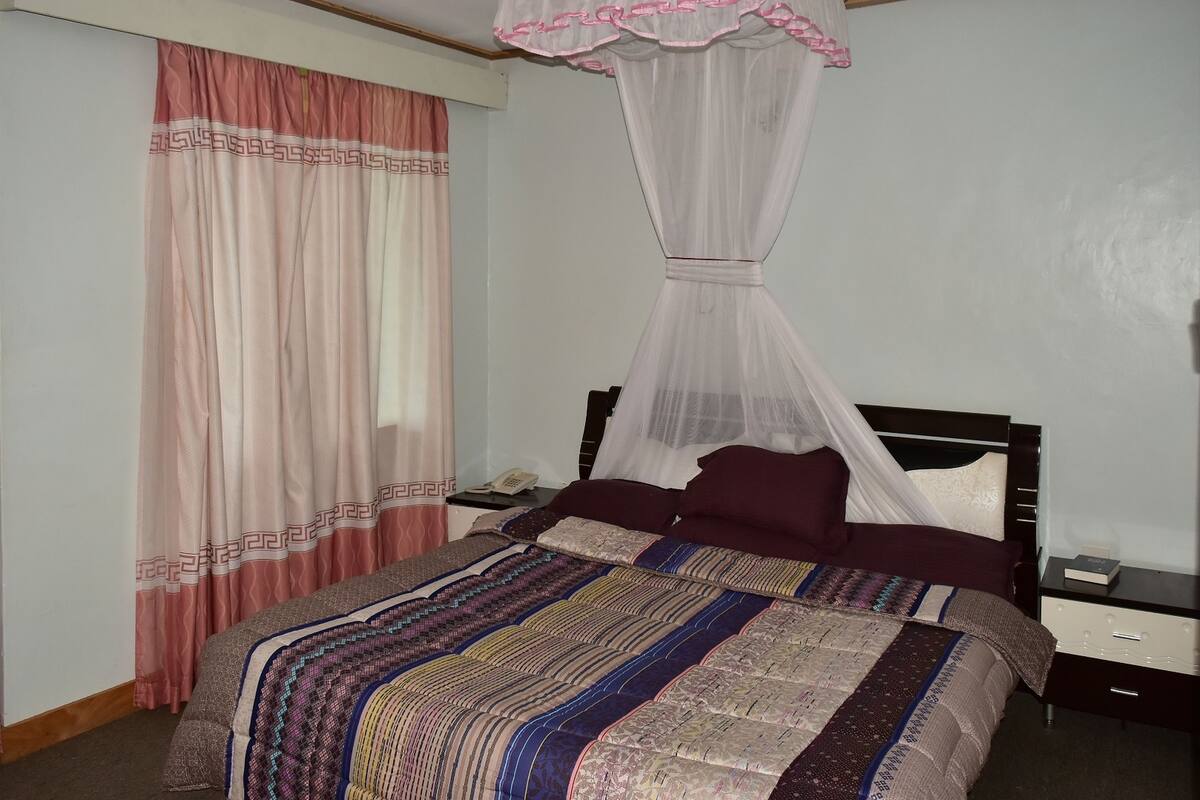 Una cama bien tendida con un edredón estampado, una mesita de noche con un teléfono y una mesita con una lámpara.