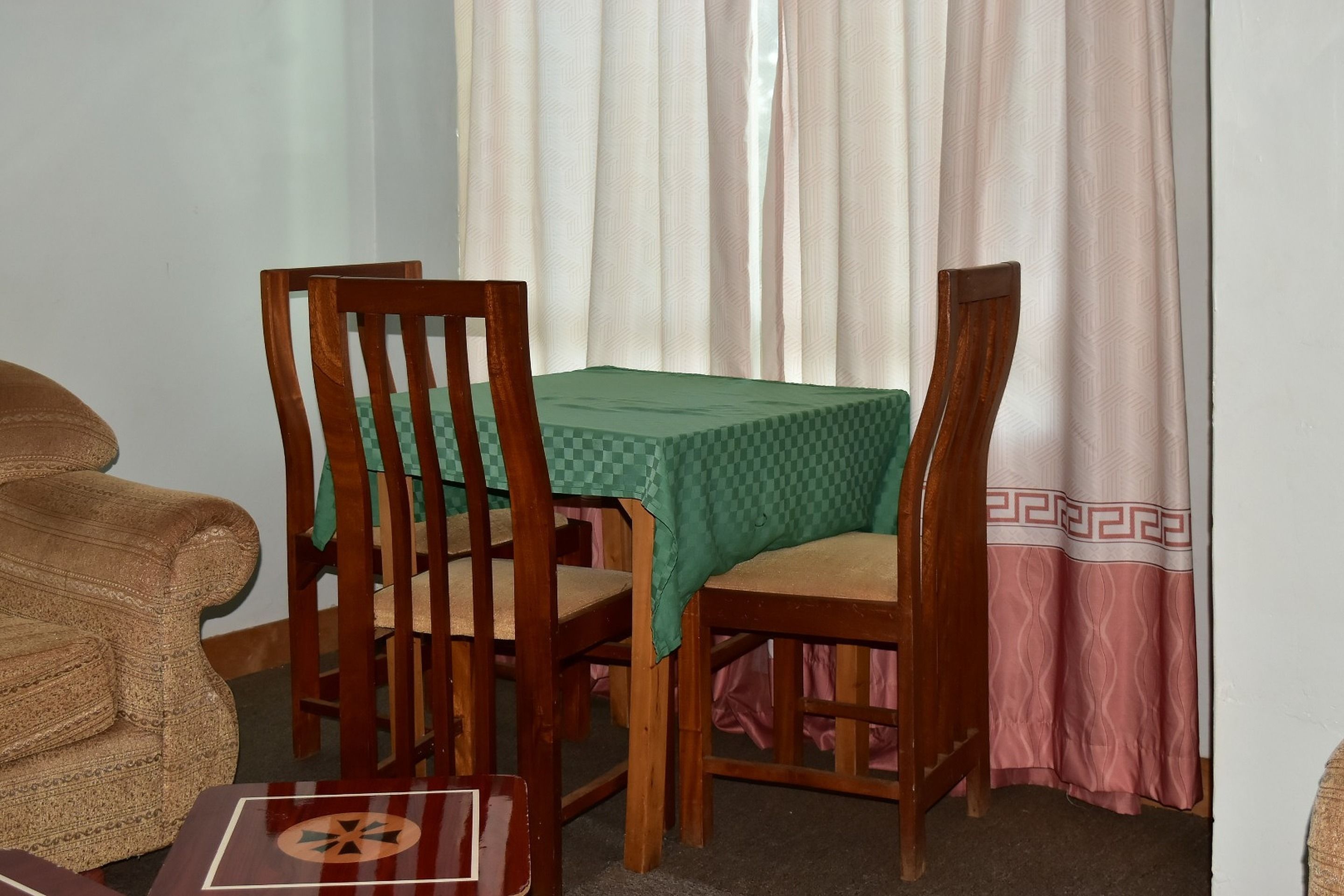 A dining area with two wooden chairs, a table with a green tablecloth, and a pink curtain.