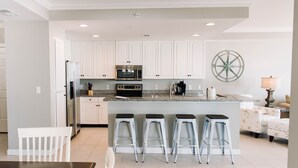 Una cocina moderna con armarios blancos, una isla central con taburetes, electrodomésticos de acero inoxidable y un adorno en la pared.
