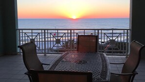 Una mesa y sillas en un balcón con vistas a la puesta de sol sobre el océano.
