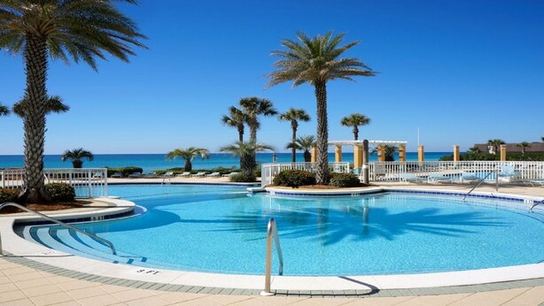 Zona de piscina con agua cristalina, palmeras y vista al océano.