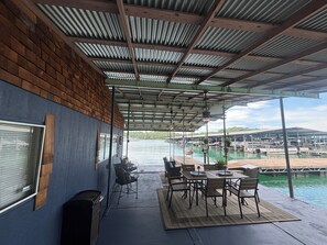A covered outdoor area with a table and chairs, a trash bin, and a view of the water and boats.
