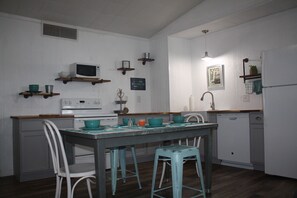 A kitchen with white cabinets, a wooden countertop, a dining table with stools, and various kitchen appliances.