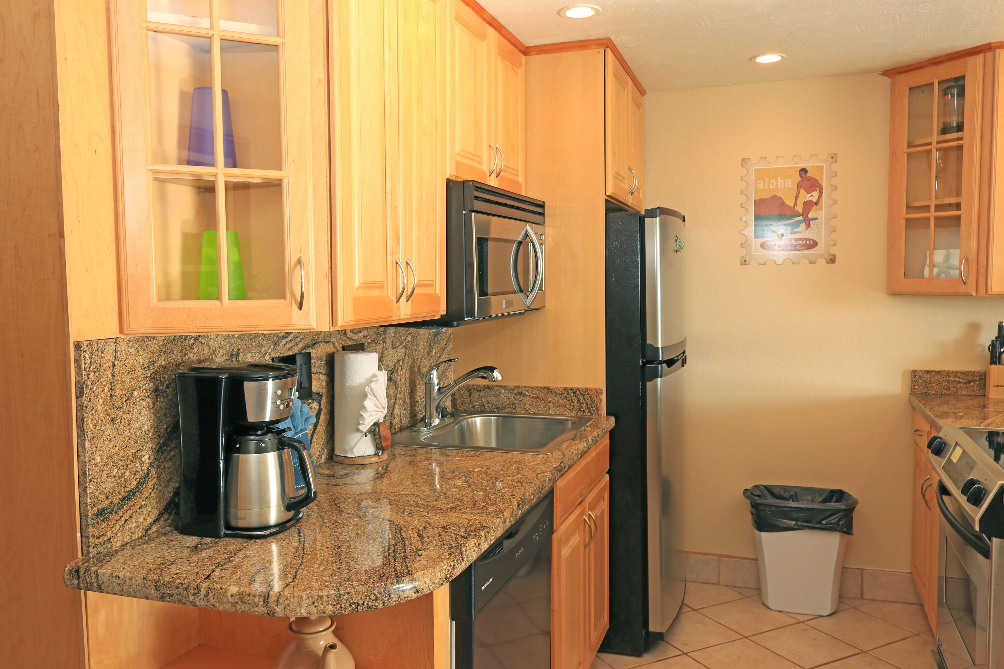 Una cocina con encimeras de granito, electrodomésticos de acero inoxidable, armarios de madera y un cubo de basura.