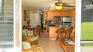 A spacious kitchen with wooden cabinets, a central island, and a dining area with wicker chairs. - Unit 108 breathtaking ocean view! discounted price! (Lahaina)