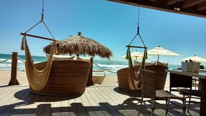 Une terrasse au bord de la plage, dotée de chaises en osier et de hamacs, avec vue sur l’océan.