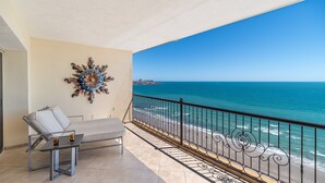 Un balcon avec vue sur l’océan, une chaise, une table et un élément décoratif mural.