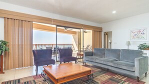 A living room with a grey sofa, two armchairs, a wooden coffee table, and a patterned rug. There is a balcony with a railing and outdoor furniture visible through the glass doors. - *Premier Host* Sonoran Sun W-609  Sun & Fun Sanctuary Spacious Oceanfront (Puerto Penasco)