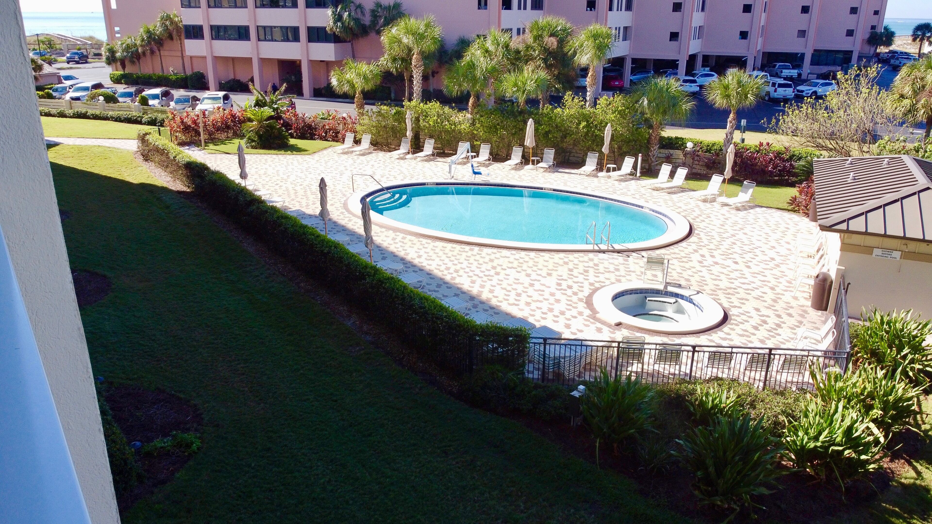 Una piscina con tumbonas y un jacuzzi, rodeada de palmeras y un edificio al fondo.