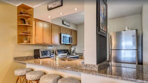 A kitchen with wooden cabinets, a stainless steel refrigerator, a microwave, and a granite countertop. - Nice to “Condo” Meet You! Vacation Fun Awaits – Islander 315 (Destin)