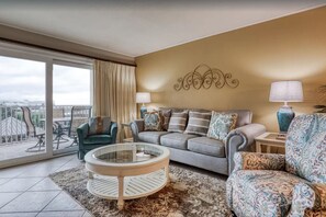 Relax in a stylish living room with a grey sofa, teal armchair, and large coffee table, surrounded by a patterned rug and offering a balcony with city views.
