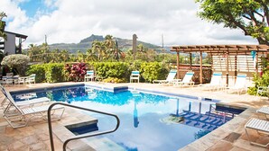 A swimming pool with lounge chairs and a pergola, surrounded by stone tiles and greenery. - Wailua Bay View 108 Oceanfront, Ground floor condo centrally located (Wailua)