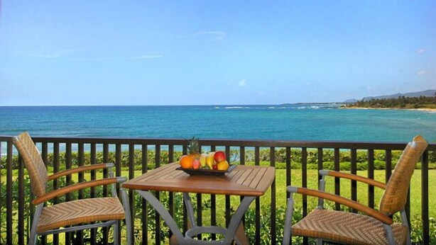 A balcony with wicker chairs and a table, overlooking a coastal view. - Wailua Bay View 108 Oceanfront, Ground floor condo centrally located (Wailua)