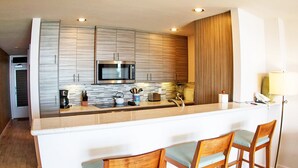 A modern kitchen with a central island, bar stools, and a microwave. - Wailua Bay View 108 Oceanfront, Ground floor condo centrally located (Wailua)