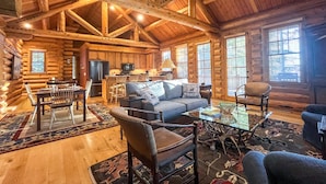 A log cabin interior with a dining area, kitchen, and living room furnished with a sofa, chairs, and a coffee table. - JHRL - Beautiful Single-Family Granite Ridge Cabin #7590, Hot Tub (Teton Village)