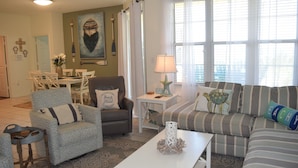 A living room with a sofa, armchairs, a coffee table, and a dining area with chairs and a table. - 105W ~ 2BR/2BA condo with Beachfront View (Gulf Shores)