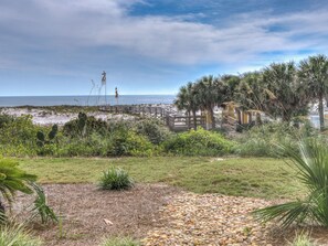 A beachside view with a wooden boardwalk, palm trees, and a grassy area with pebbles.