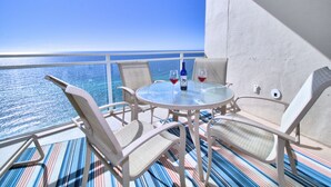 Un balcon avec une table en verre, des chaises blanches et une bouteille de vin rouge.