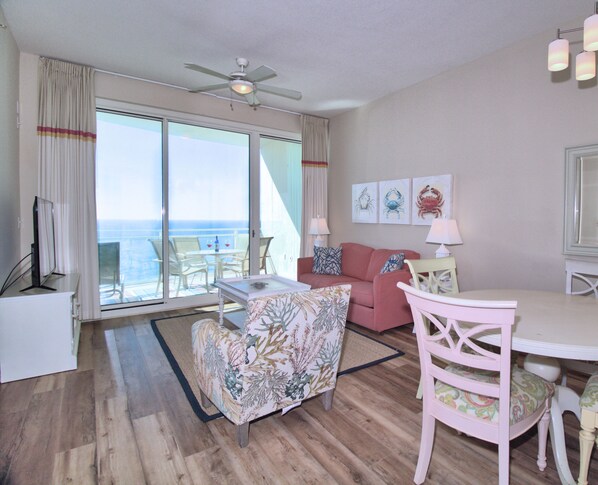 A room with a balcony, a ceiling fan, a dining table with chairs, a sofa, and artwork on the wall.