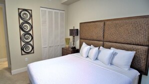 A bedroom with a large bed, a headboard, a nightstand with a lamp, a wall-mounted artwork, and a closet with louvered doors. - 2305 - Gulf Front Living with Breathtaking Views (Panama City Beach)