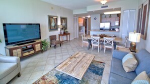 A living room with a television, sofa, and coffee table. There is a dining area with a table and chairs. - 2305 - Gulf Front Living with Breathtaking Views (Panama City Beach)