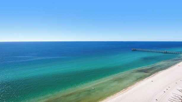 Una playa con agua turquesa cristalina, una orilla de arena y un muelle de madera que se adentra en el mar.