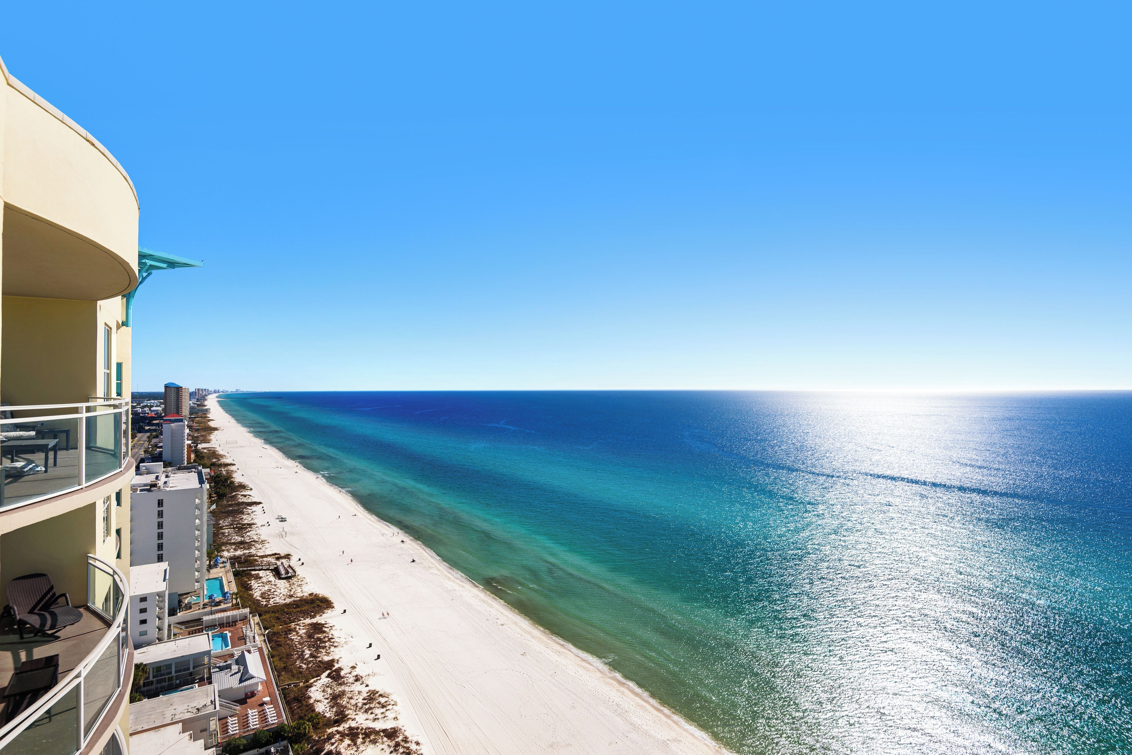 A beachfront hotel with balconies overlooking the ocean, a pool area, and a sandy beach.