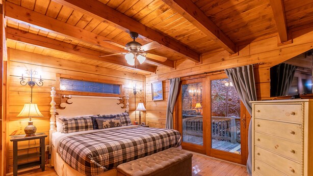 Ein gemütliches Schlafzimmer in einer Holzhütte mit einem Bett, einer Bank, einem Schminktisch und einem Deckenventilator.