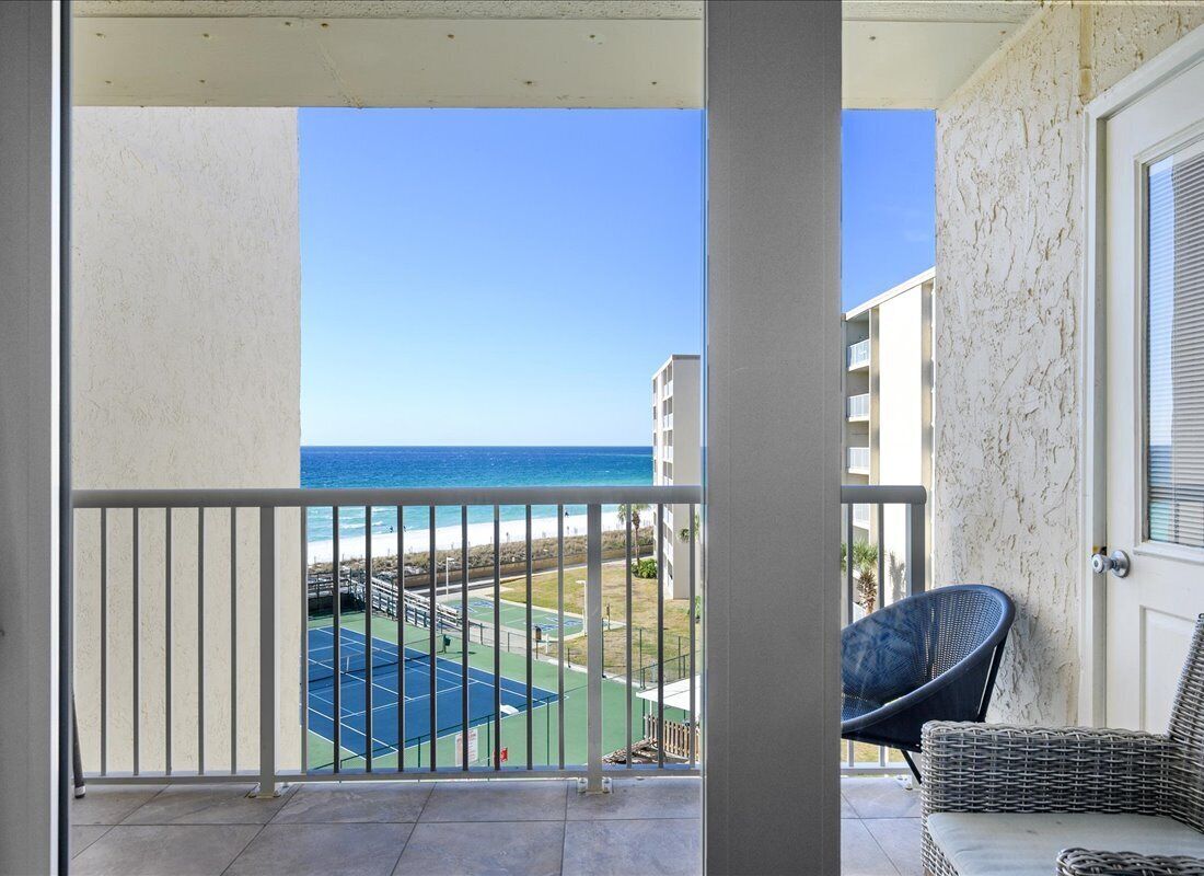 A balcony with a view of the beach and tennis court.