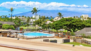 Een resort met een zwembad, palmbomen en een berg op de achtergrond.