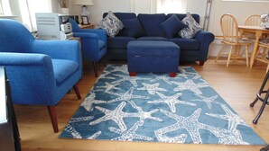 Ein Wohnzimmer mit blauem Sofagarnitur, passendem Ottomanen und einem Teppich mit Seestern-Muster.