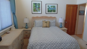 Un dormitorio con una cama, dos mesitas de noche, un aparador y dos cuadros en la pared.
