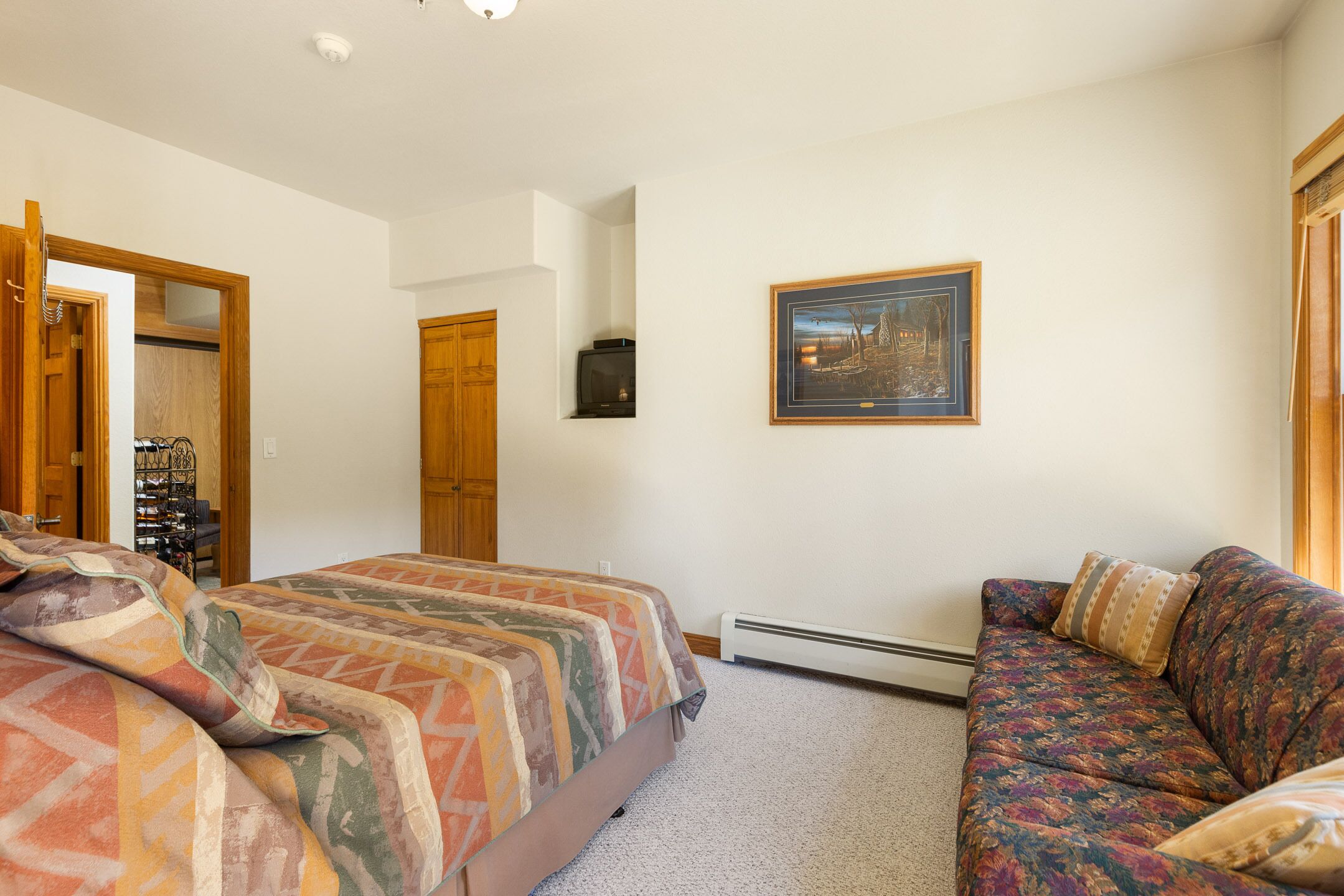 A bedroom with a bed, a sofa, a framed picture on the wall, and a door leading to another room.