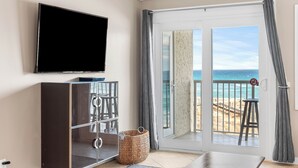 Ett rum med en TV, en skjutdörr i glas som leder ut till stranden, ett litet bord och en korg av rotting.