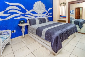 A bedroom with a bed, a nightstand, a chair, and a wall with a blue and white design.