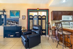Uma sala de estar com um sofá de couro preto, uma área de jantar com banquetas, uma cozinha com micro-ondas e uma porta decorativa com design de mapa.