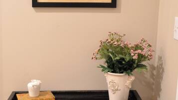 Un journal encadré accroché au mur, une petite table avec une plante, un objet décoratif et un pichet en argent.