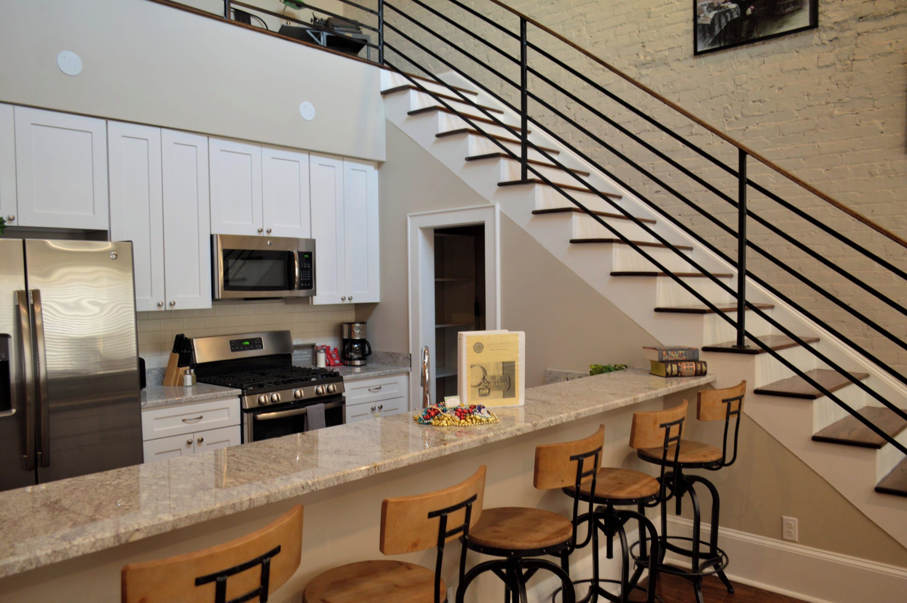 A modern kitchen with stainless steel appliances, a marble countertop, and a bar area with stools.
