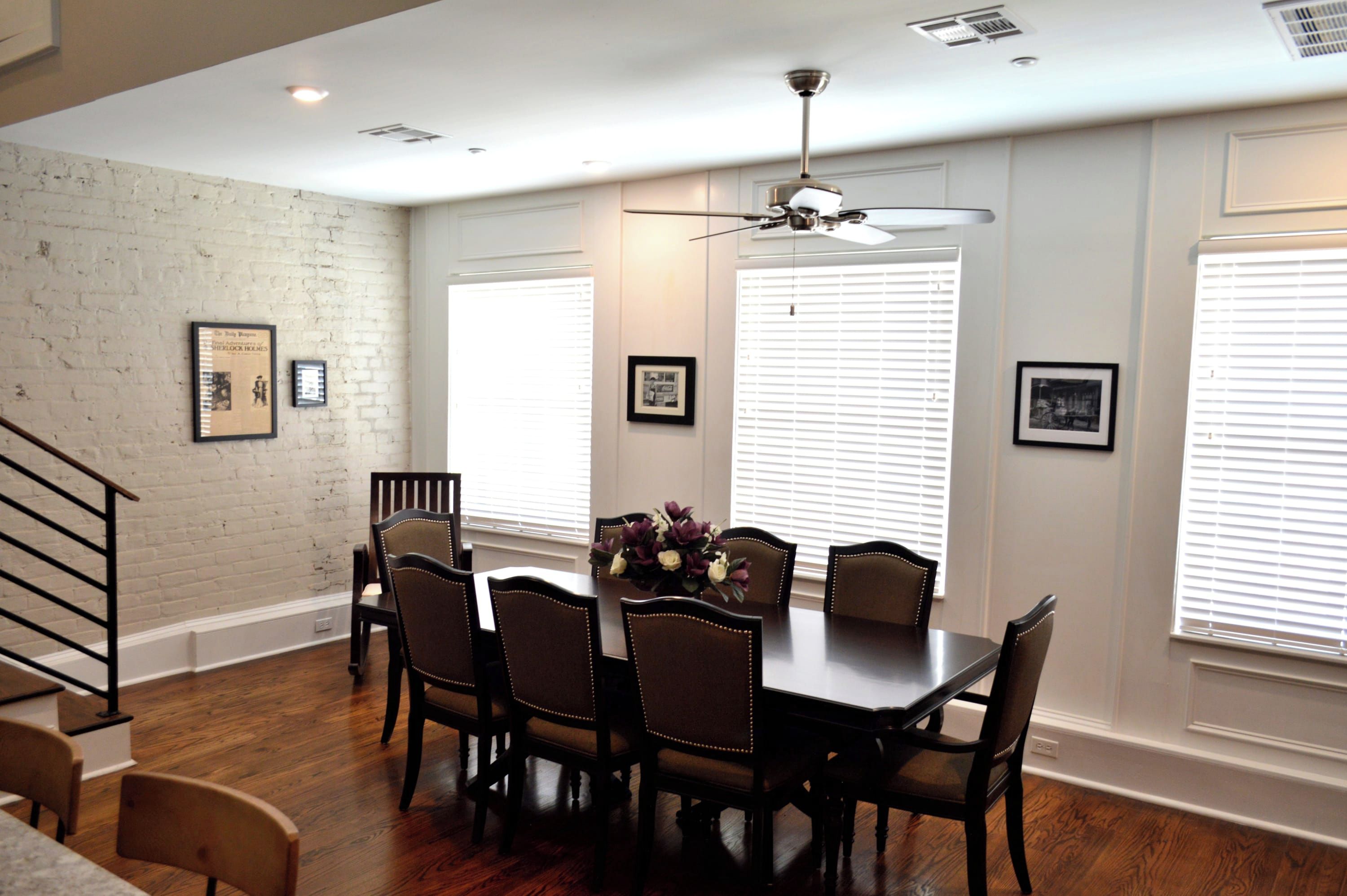 A dining area with a wooden table and chairs, a ceiling fan, and framed pictures on the walls.