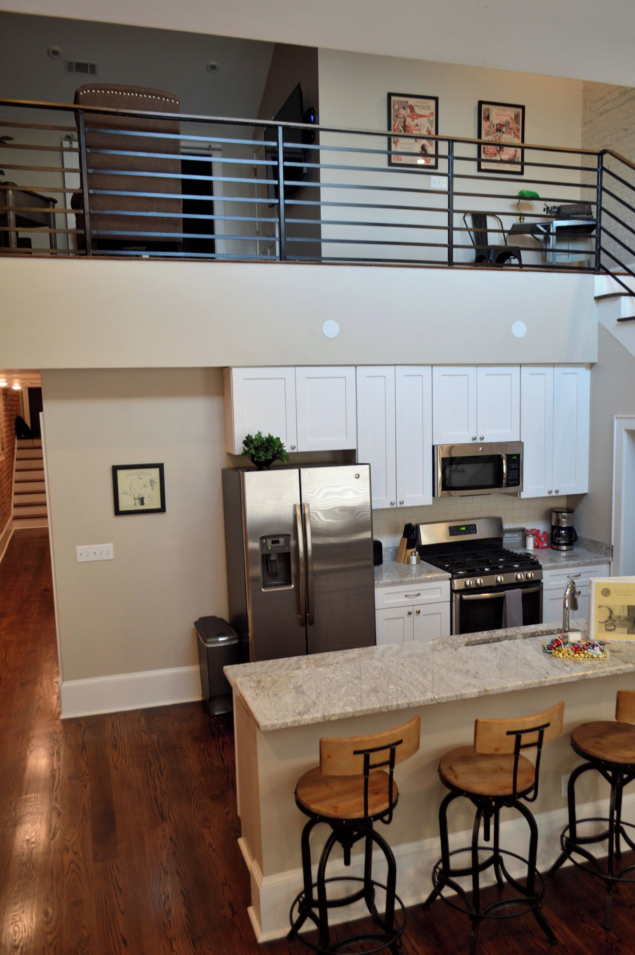 A modern kitchen with a stainless steel refrigerator, microwave, and stove, a two-tiered bar area with bar stools, and a staircase leading to an upper level.