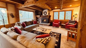 A cozy cabin interior with a fireplace, wooden beams, a sofa, and a red armchair. - Trailside Home on Alpen Trail with Hot Tub & Allows Dogs (Bessemer)