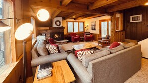 A cozy living room with a fireplace, wooden ceiling beams, and a large window. - Trailside Home on Alpen Trail with Hot Tub & Allows Dogs (Bessemer)