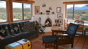 A cozy living room with a fireplace, a sofa, a dining table, and a view of the desert landscape.
