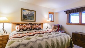 Camera da letto ordinata con un letto, due lampade da comodino, un quadro incorniciato, una finestra con tende e un baule di legno.