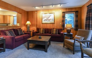 A cozy living room with wooden paneling, a large painting, a sofa, a coffee table, and a chair.